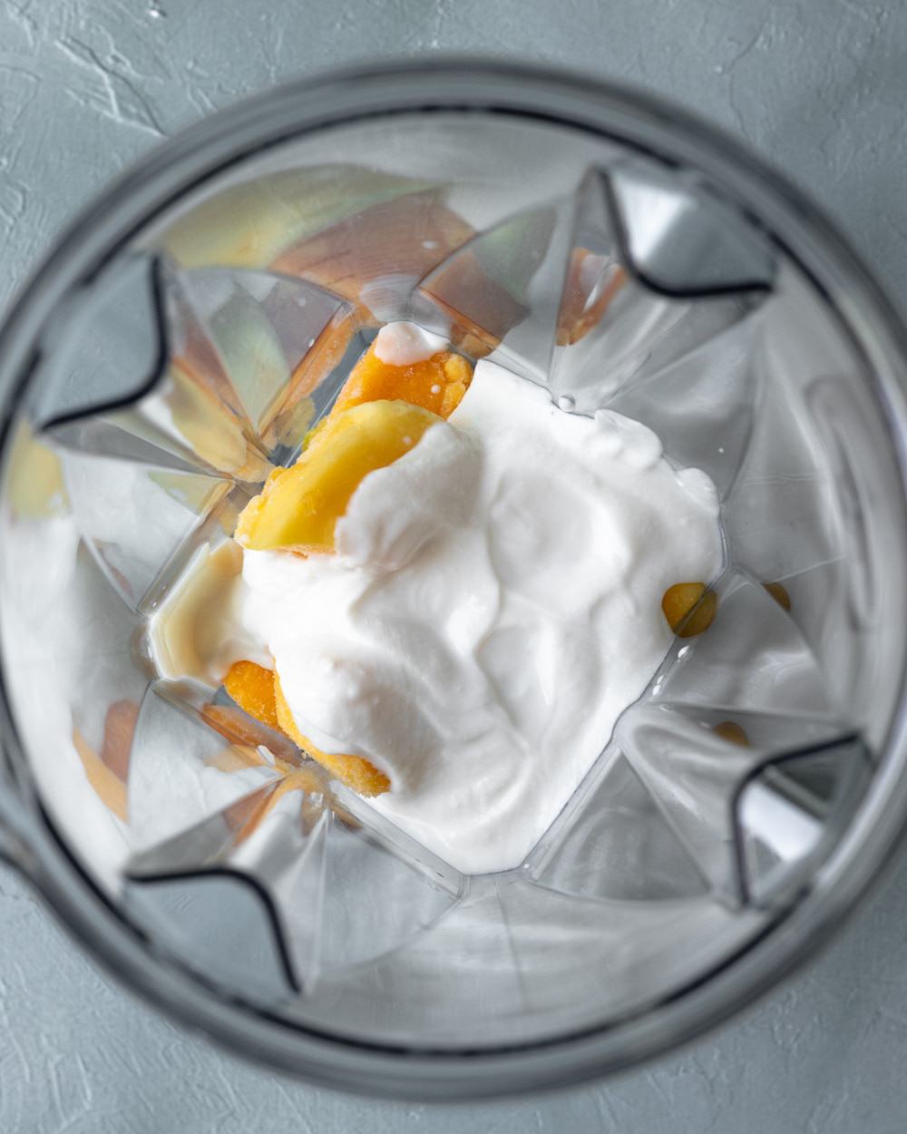 looking inside blender jar with creamy cashew yogurt poured over mango.