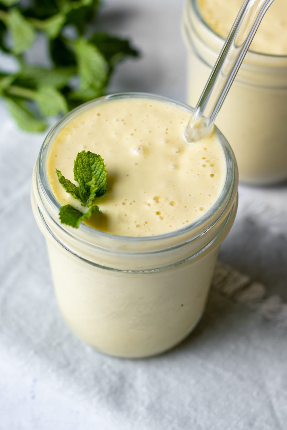 creamy mango smoothie in a glass garnished with mint.