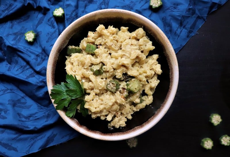 overhead view of mac and cheese in a stoneware bowl with sliced okra scattered on table.