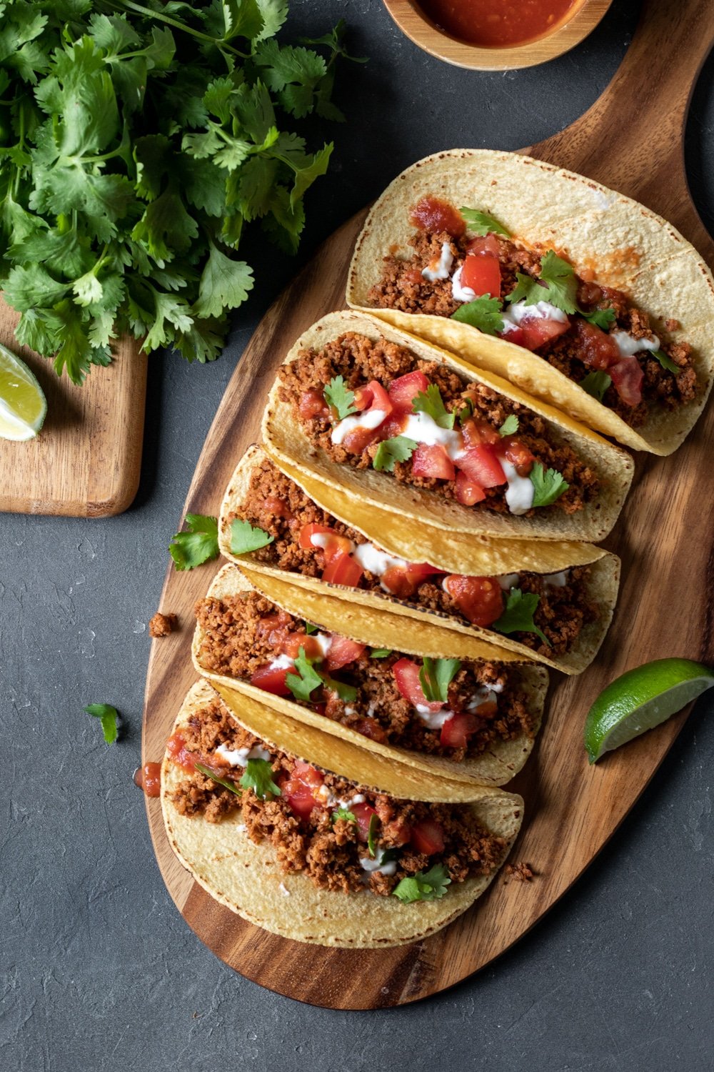 overhead view of five vegan tacos lined up on a wooden board.