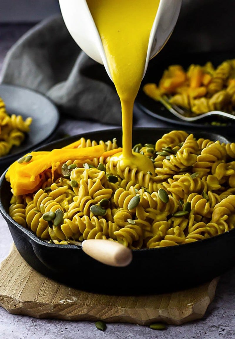 pouring orange pumpkin cheese sauce onto pasta.