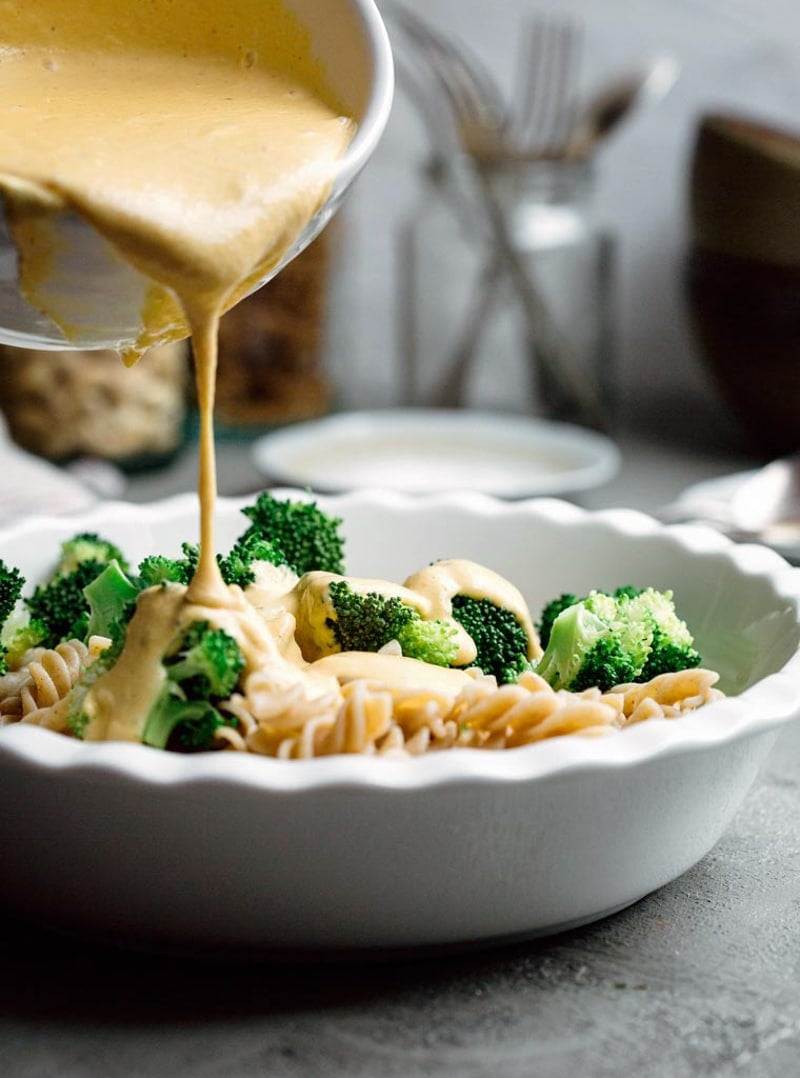 pouring creamy sauce onto pasta and broccoli.