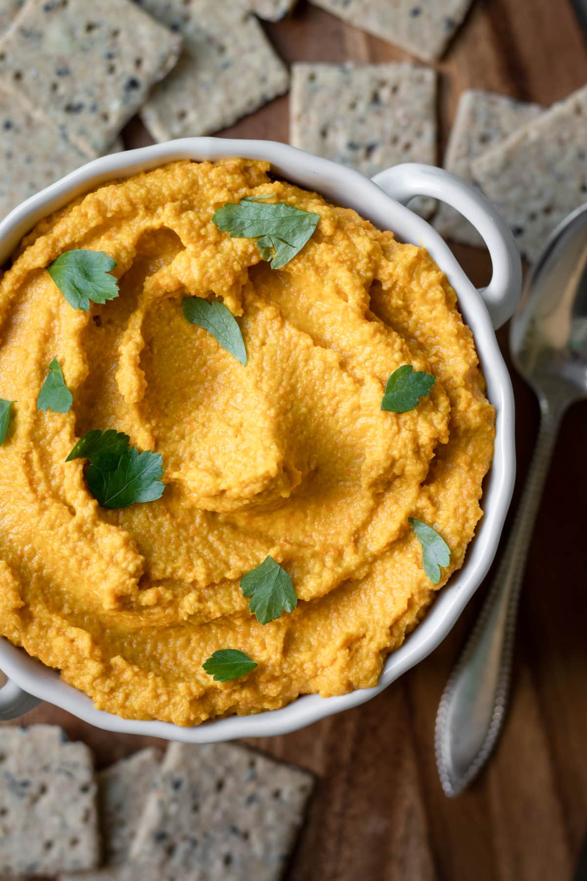 overhead shot of hummus in a white bowl surrounded by crackers.