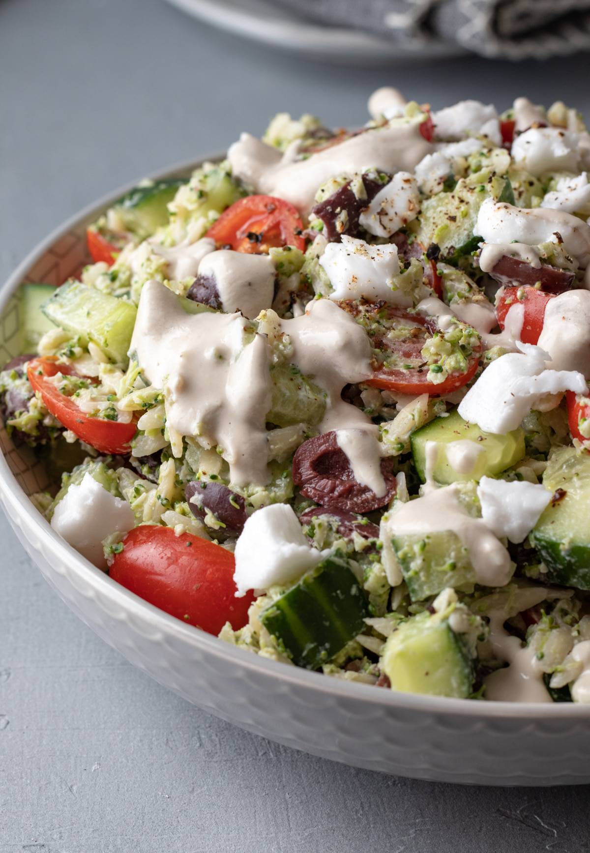 close up view of bowl full of vegan orzo salad with colorful vegetables.