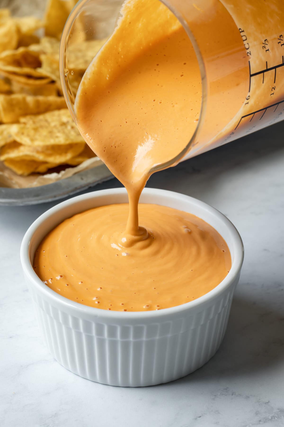 Pouring creamy vegan cheese sauce into a small white bowl.