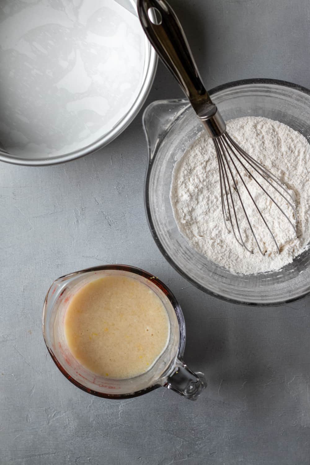 a cake pan lined with parchment and two separate bowls containing wet and dry ingredients.