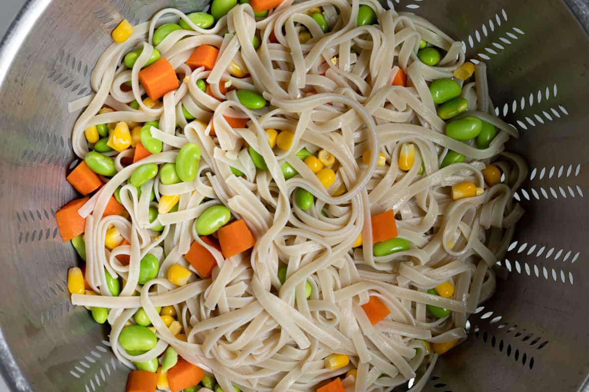 noodles, carrot, edamame, and corn draining in a colander