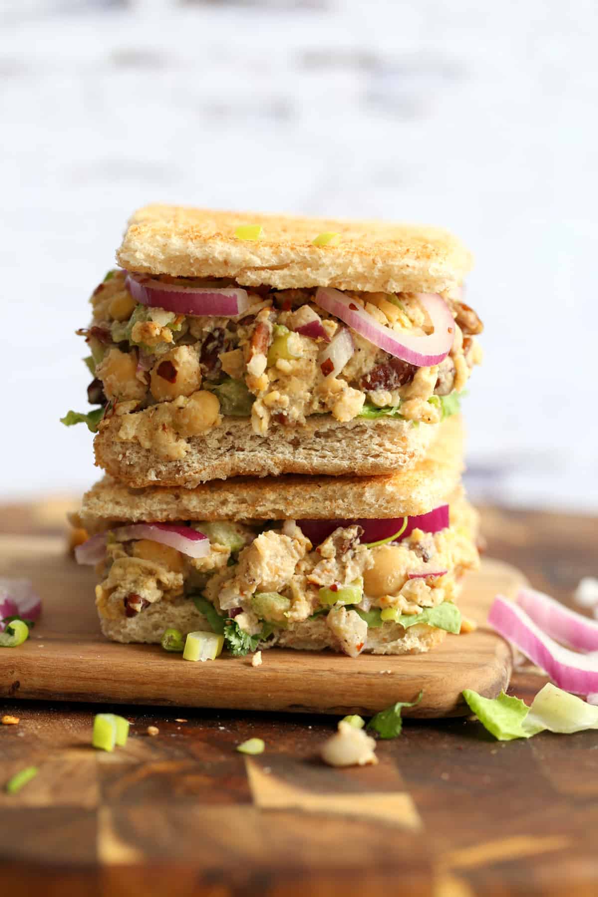 two thick sandwiches stacked on a cutting board.