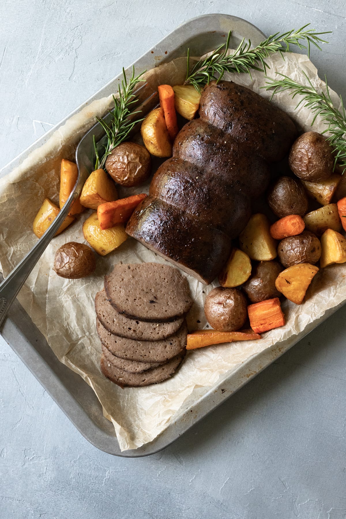 vegan holiday roast on a platter with roasted vegetables and rosemary.