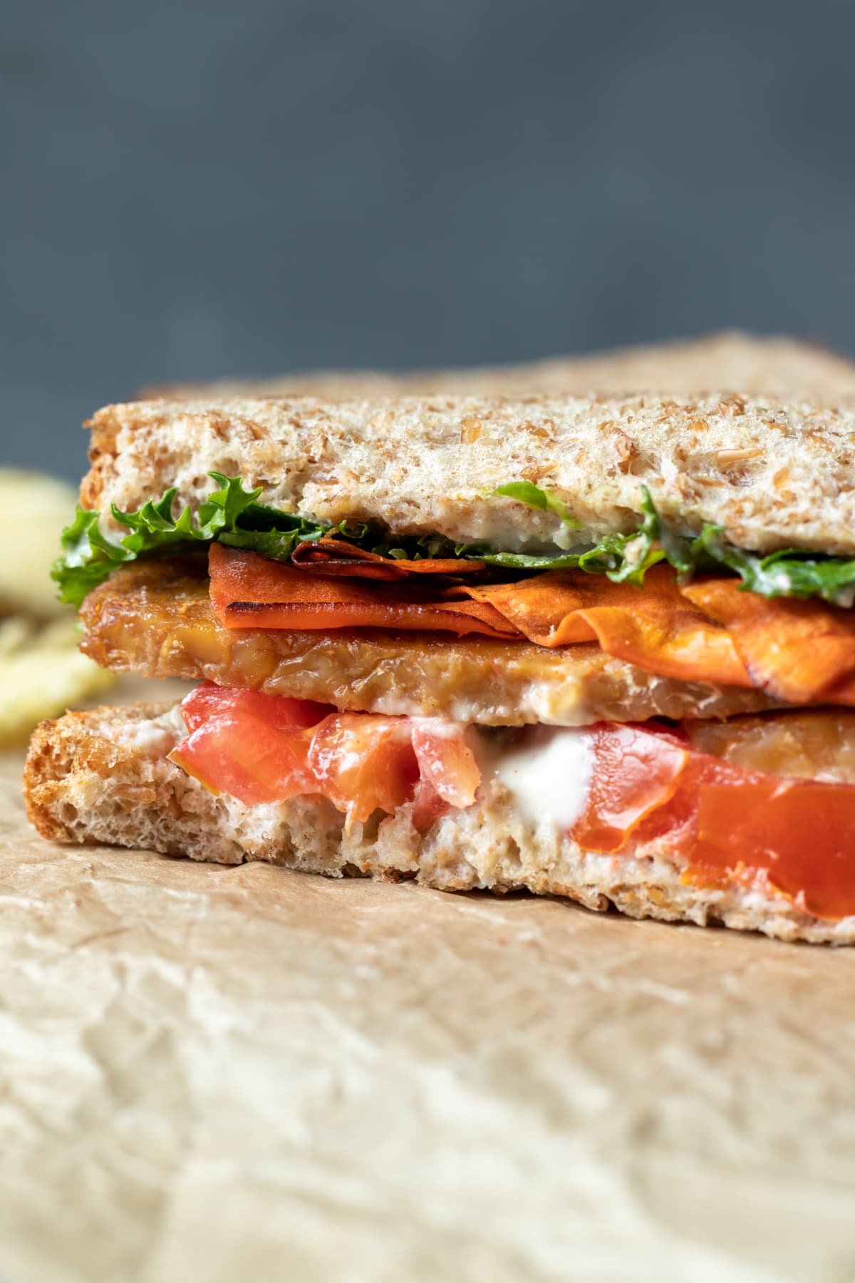 side view of inside of sandwich showing mayo, tomato, lettuce, and 2 kinds of vegan bacon.