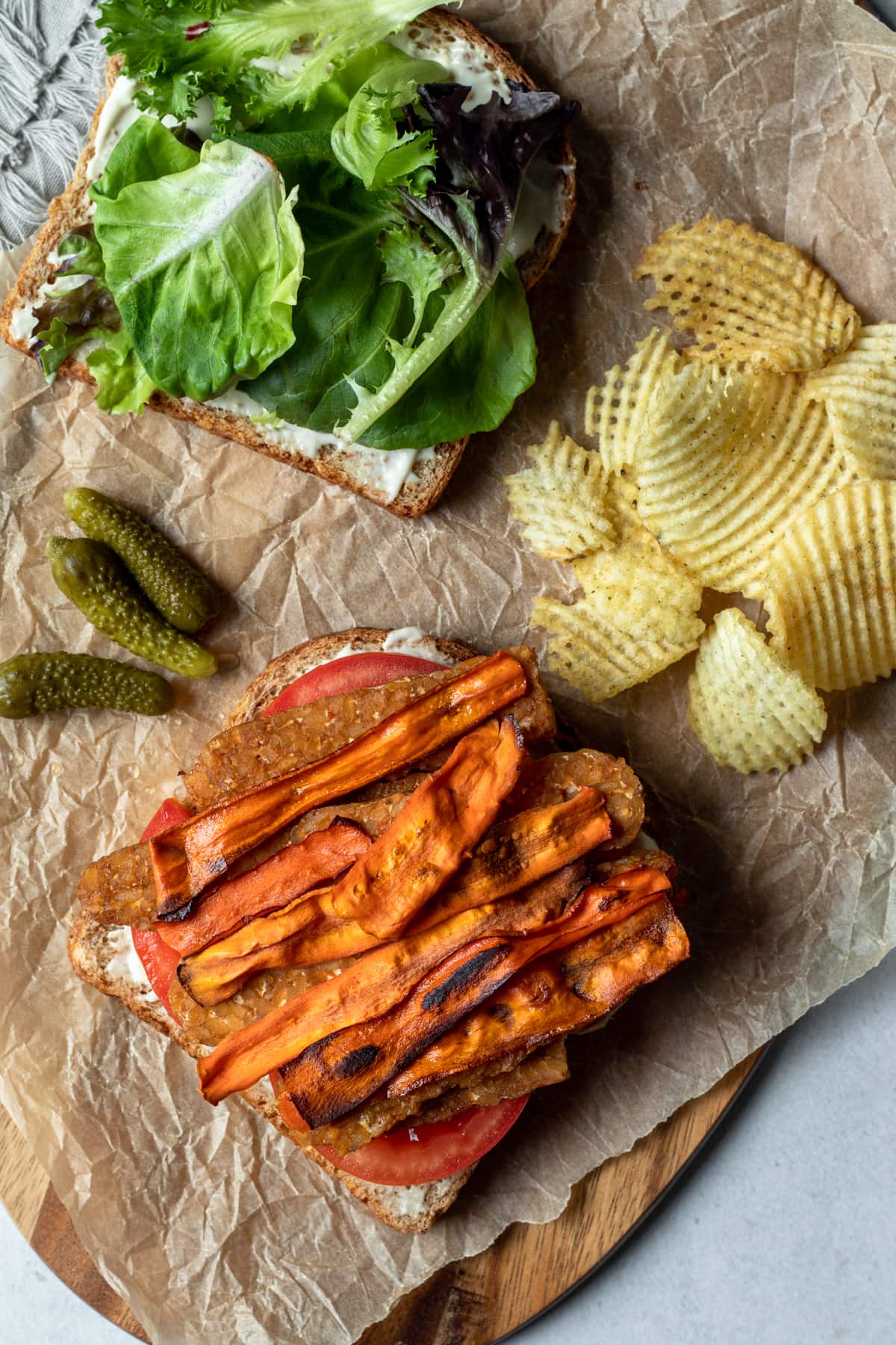 overhead view of open face vegan BLT with chips and pickles on the side.