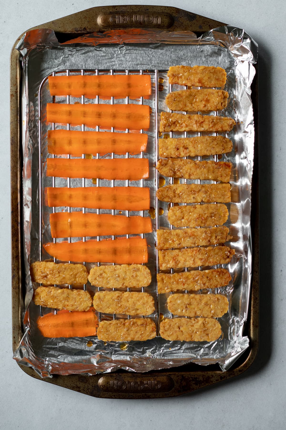 tempeh and carrot lined up on a rack on a baking sheet.