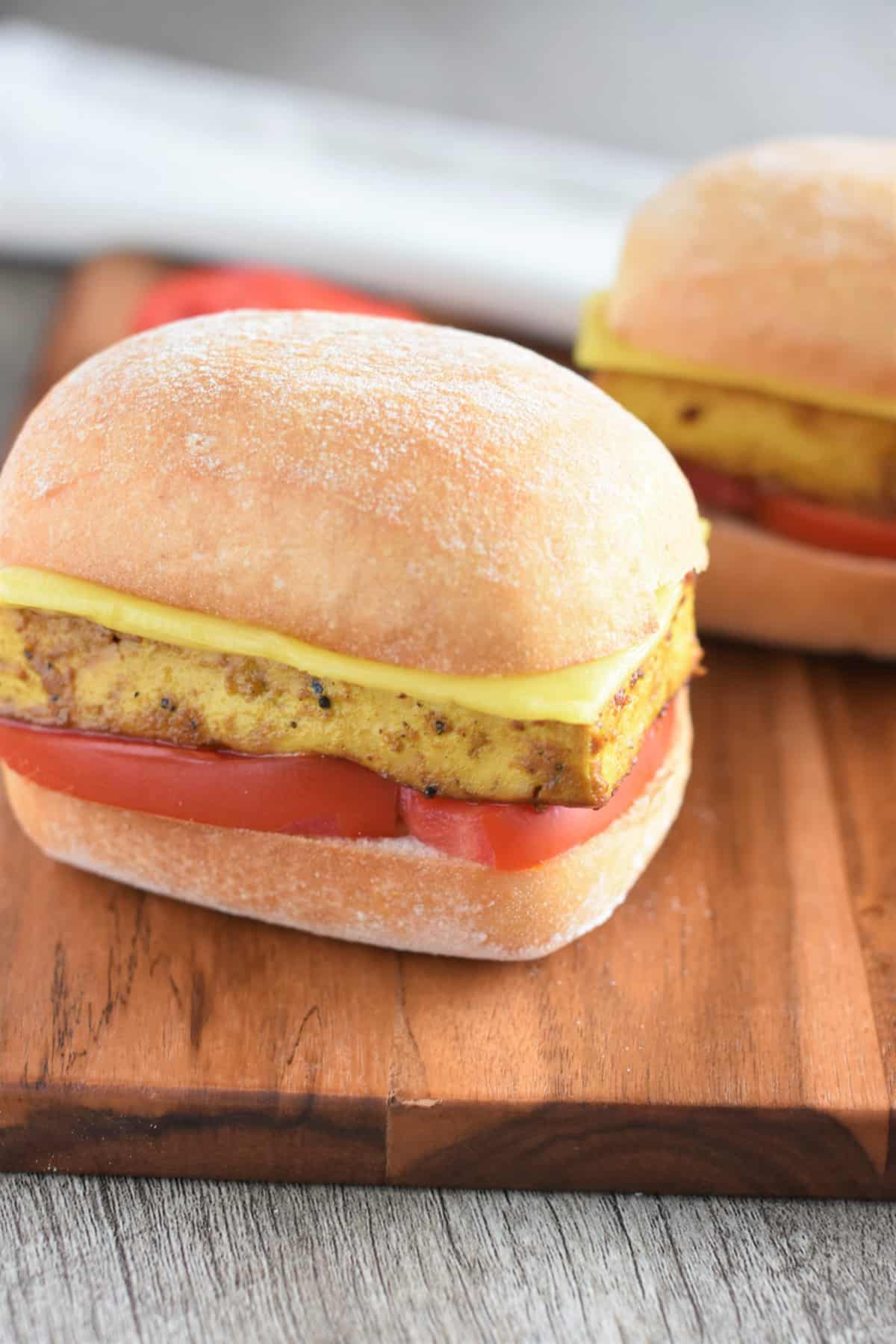 close up of two breakfast sandwiches on a wooden board.