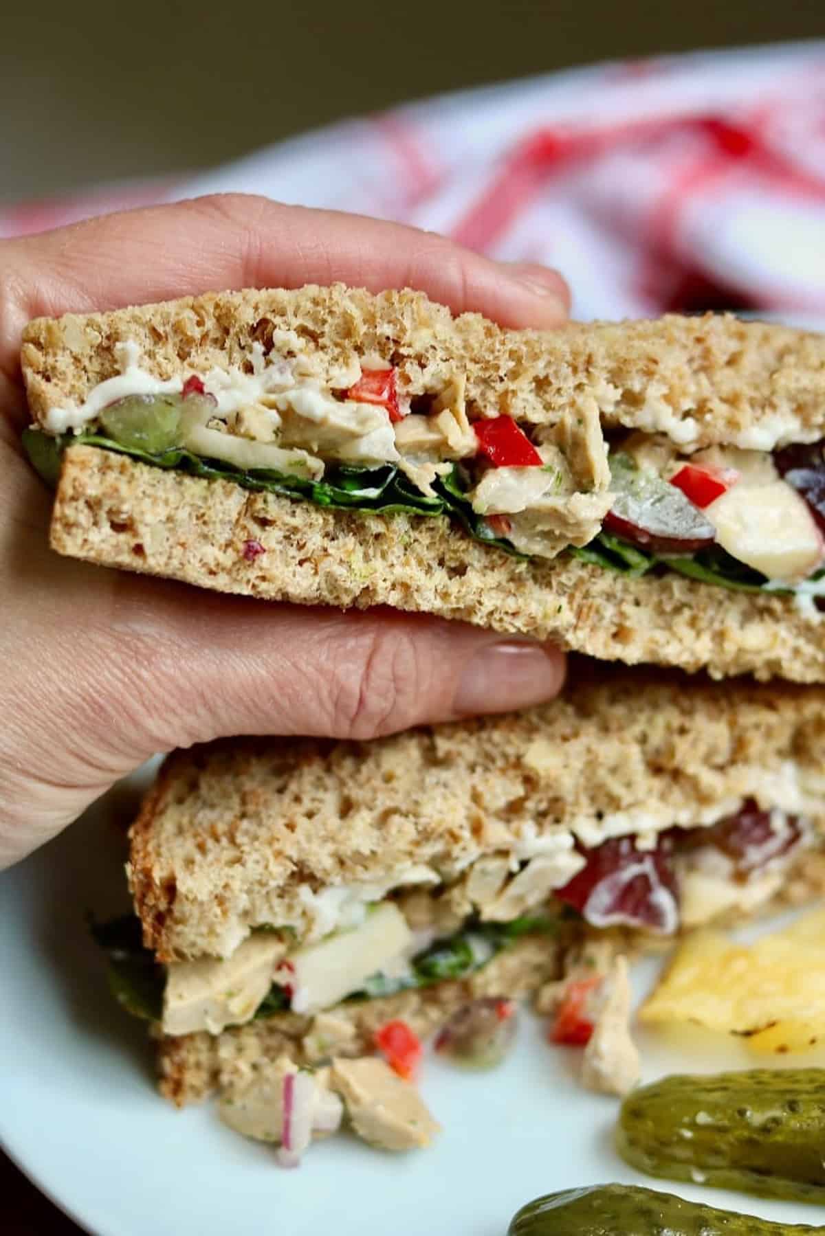 close up of a hand holding one half of a vegan chicken salad sandwich.
