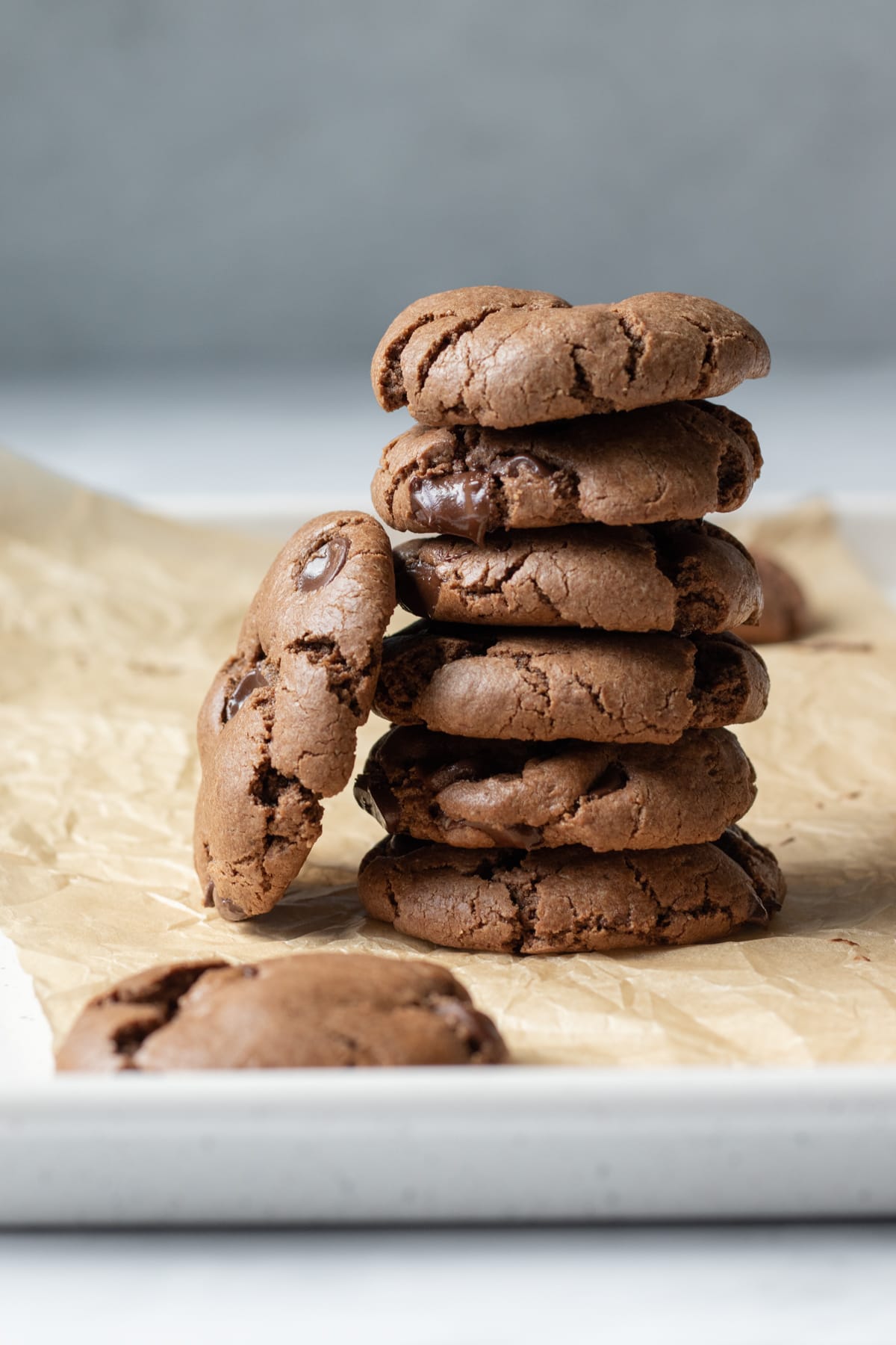 6 chocolate oat flour cookies stacked and resting on a parchment-lined baking sheet.