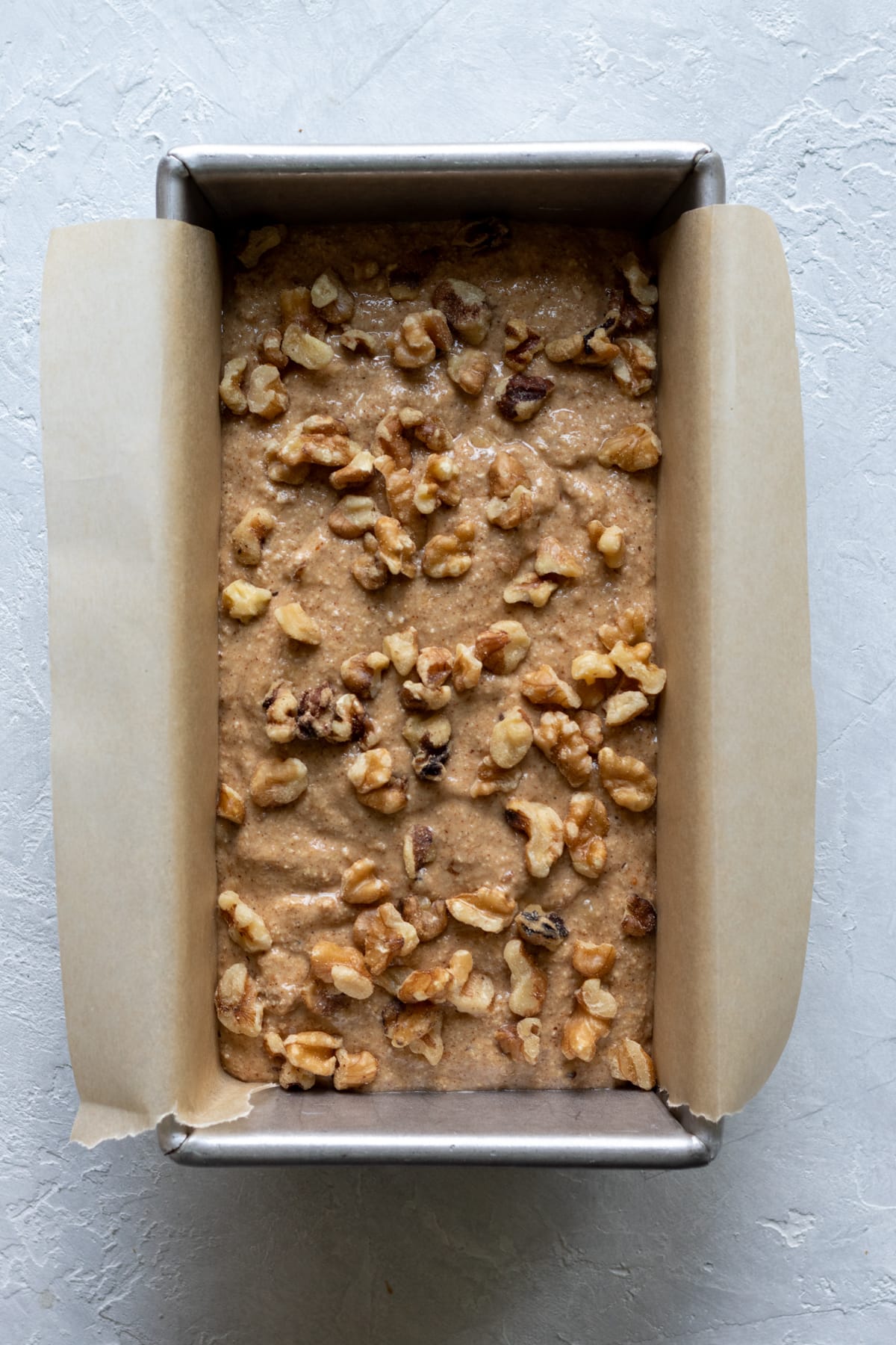 banana bread batter in parchment lined pan sprinkled with walnuts.