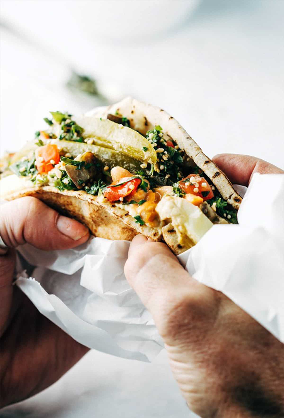 hands holding a colorful pita sandwich.