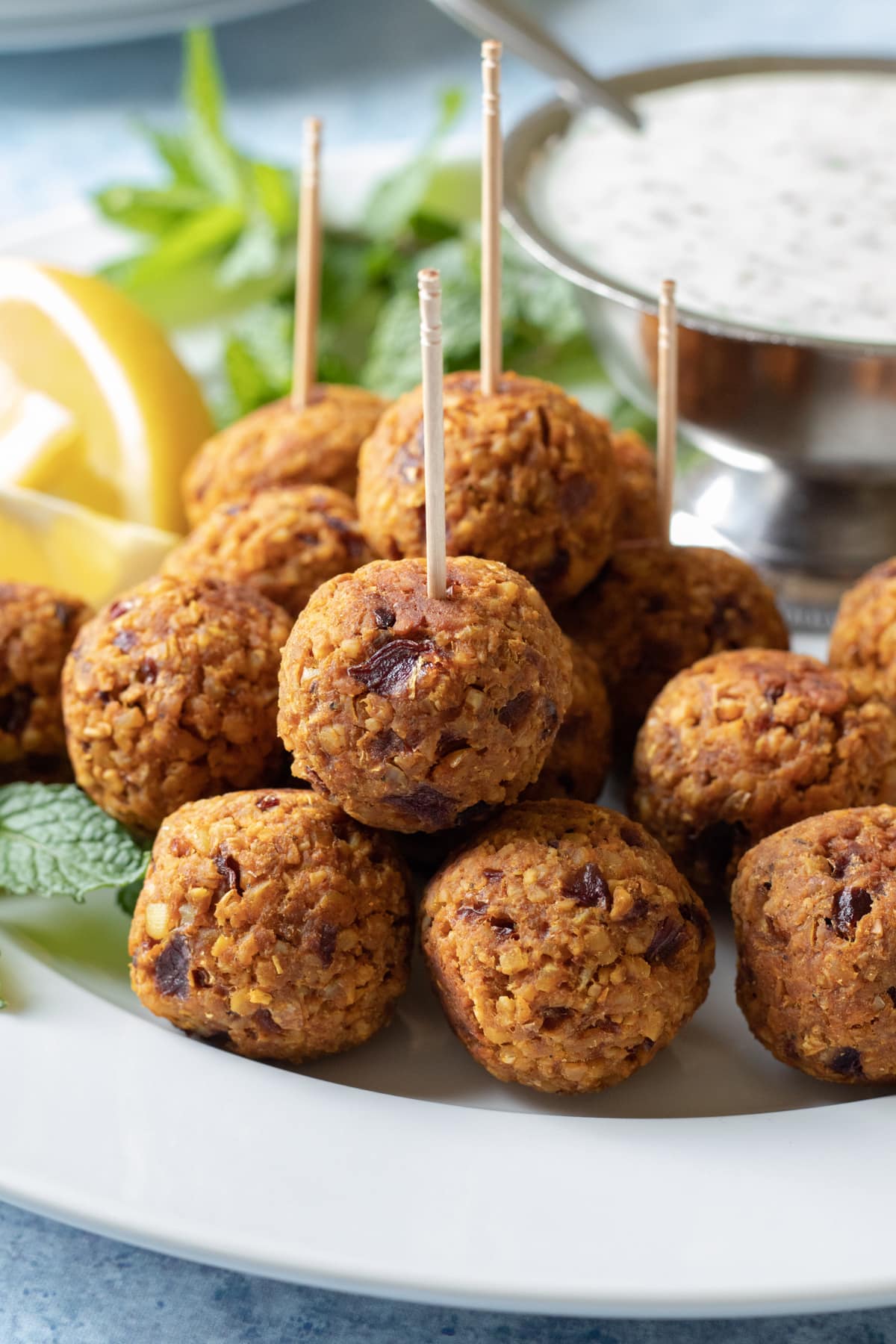 tempeh meatballs stacked on a serving platter served with yogurt sauce and lemon wedges.