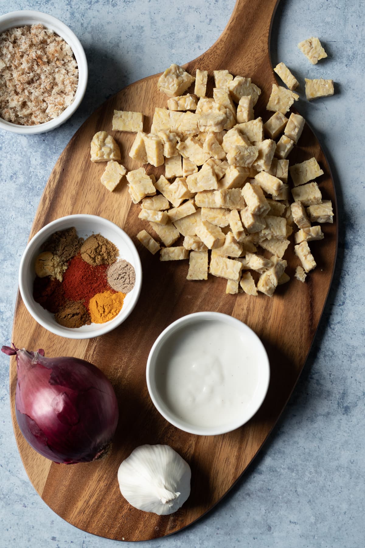 ingredients laid out on a wooden board - tempeh, onion, spices, yogurt, garlic, breadcrumbs.