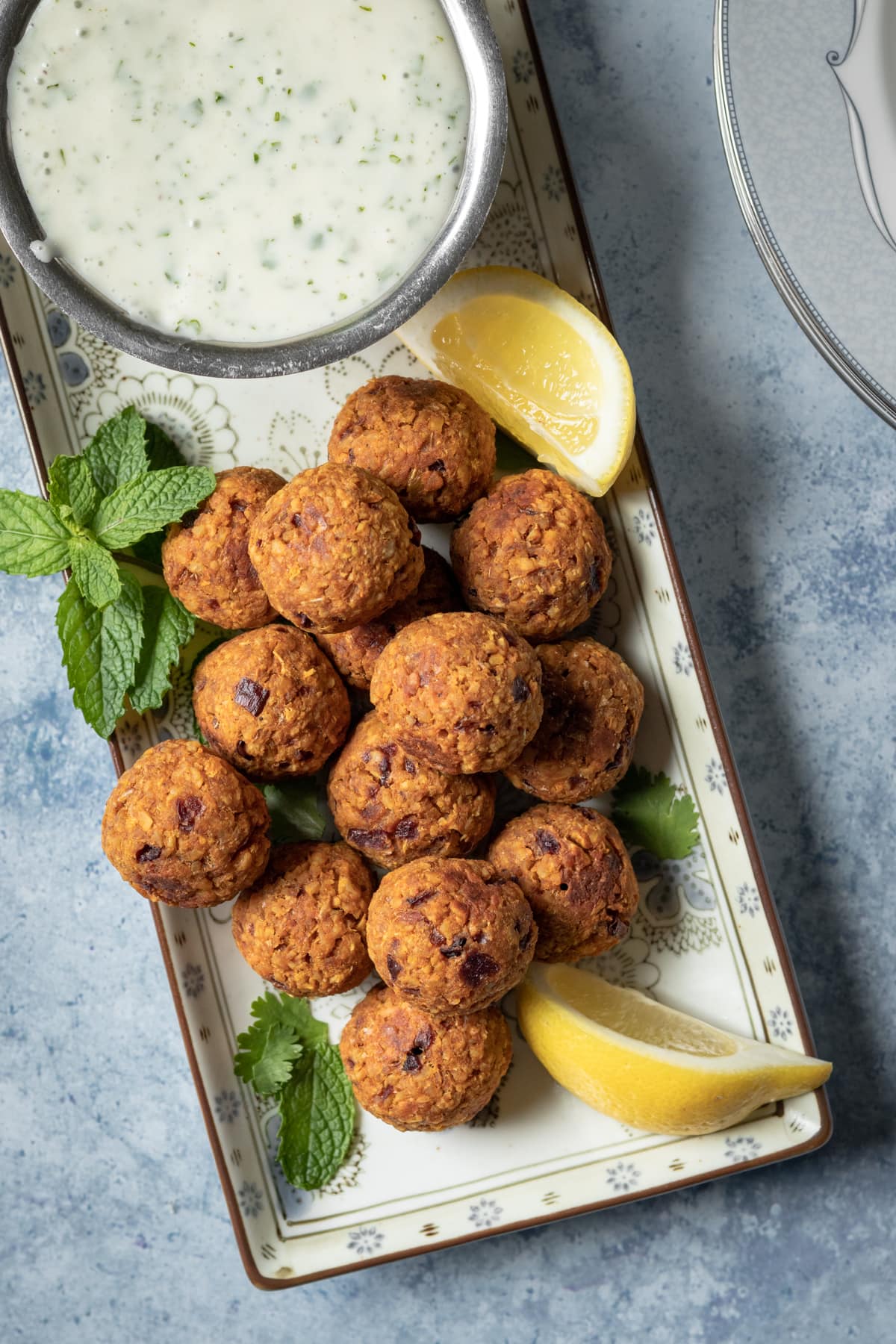 overhead shot of baked meatballs on a platter, with a bowl of cilantro-yogurt sauce.