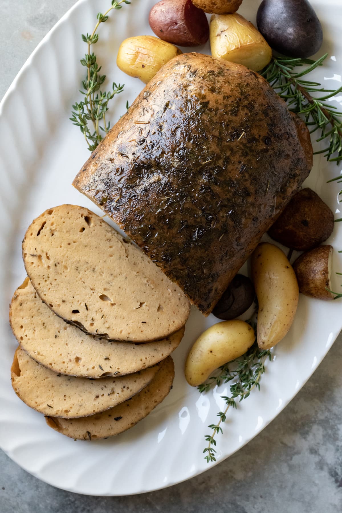 seitan turkey roast on a platter with fresh herbs and roasted potatoes.