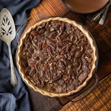 overhead view of whole vegan pecan pie on a dark wood grain table.