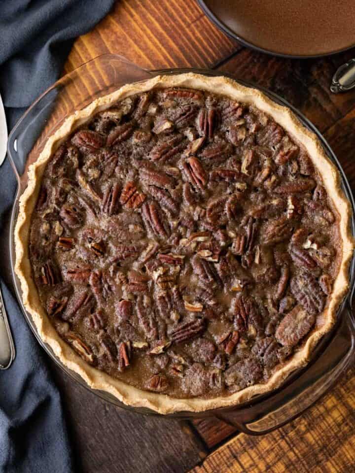 overhead view of whole vegan pecan pie on a dark wood grain table.