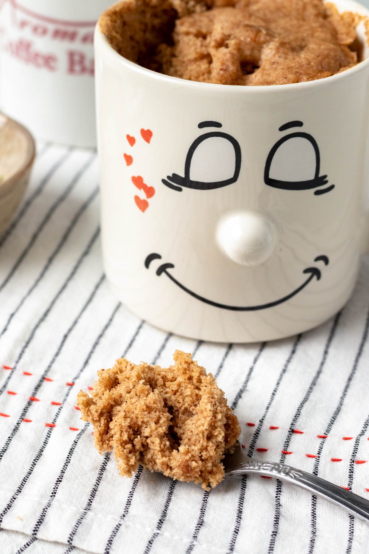 A spoonful of oatmeal mug cake resting in front of a mug.