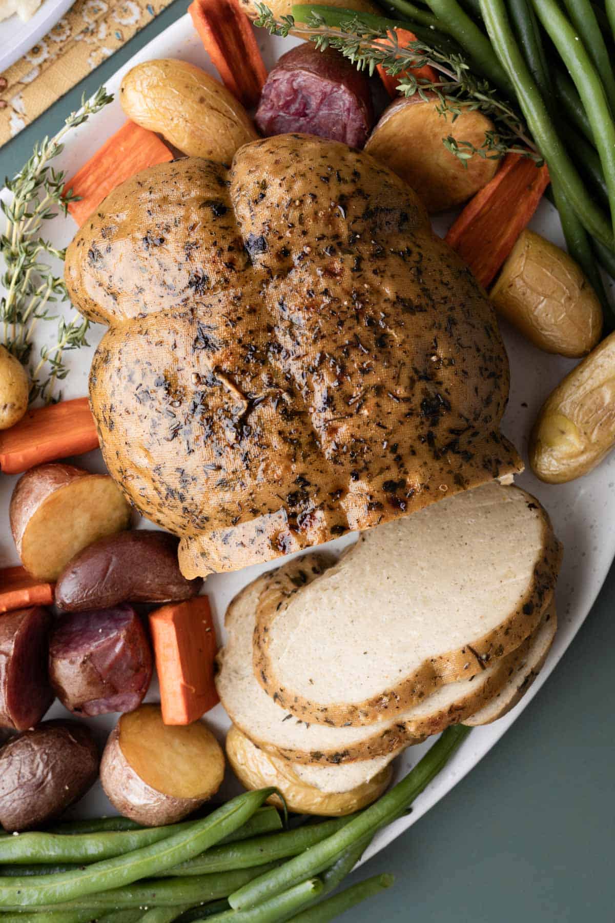 Whole vegan turkey on a platter with slices cut to show texture, surrounded by roasted vegetables.