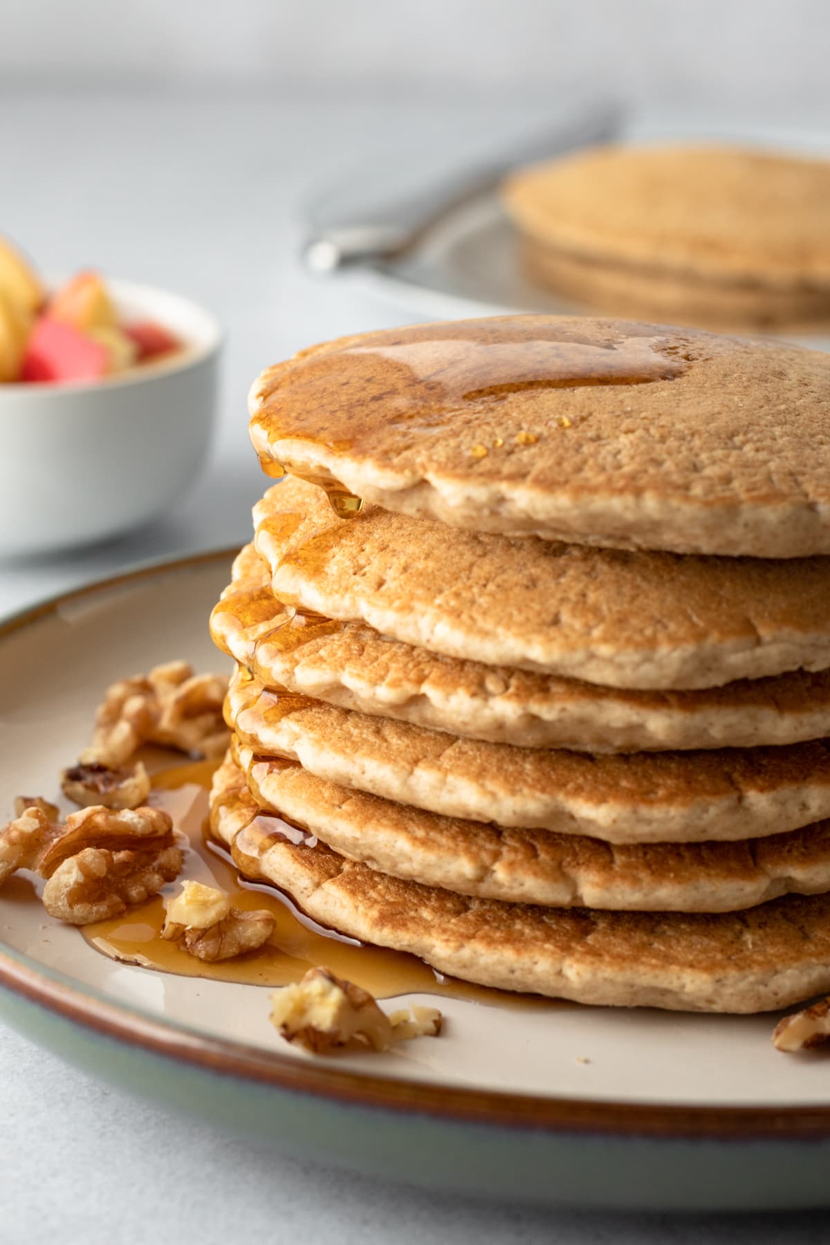 a stack of oat pancakes with walnuts and maple syrup.