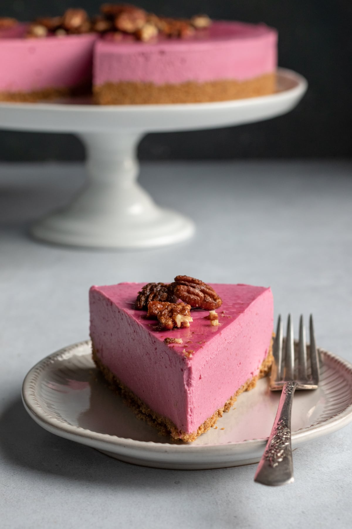 a slice of pink cranberry cheesecake on a plate with cake in background