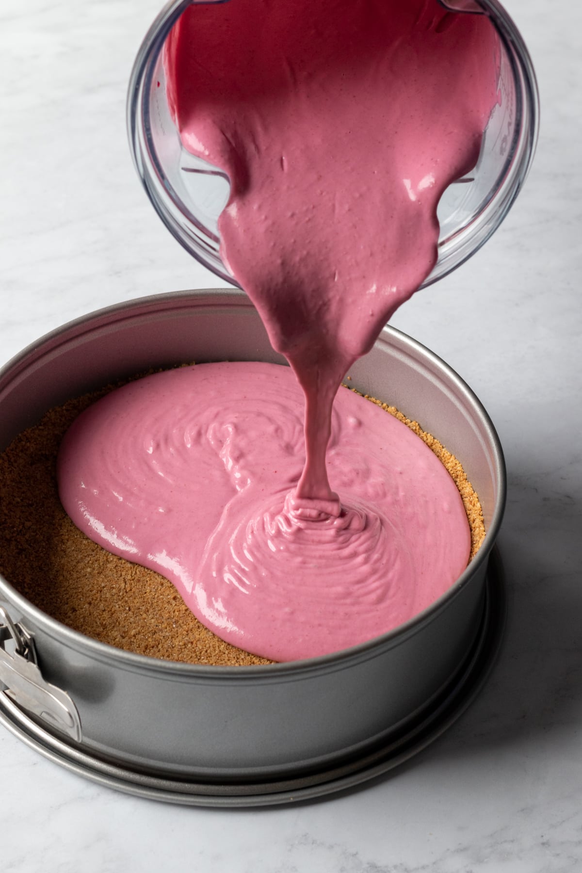 pouring blended cranberry cheesecake filling into the springform pan.