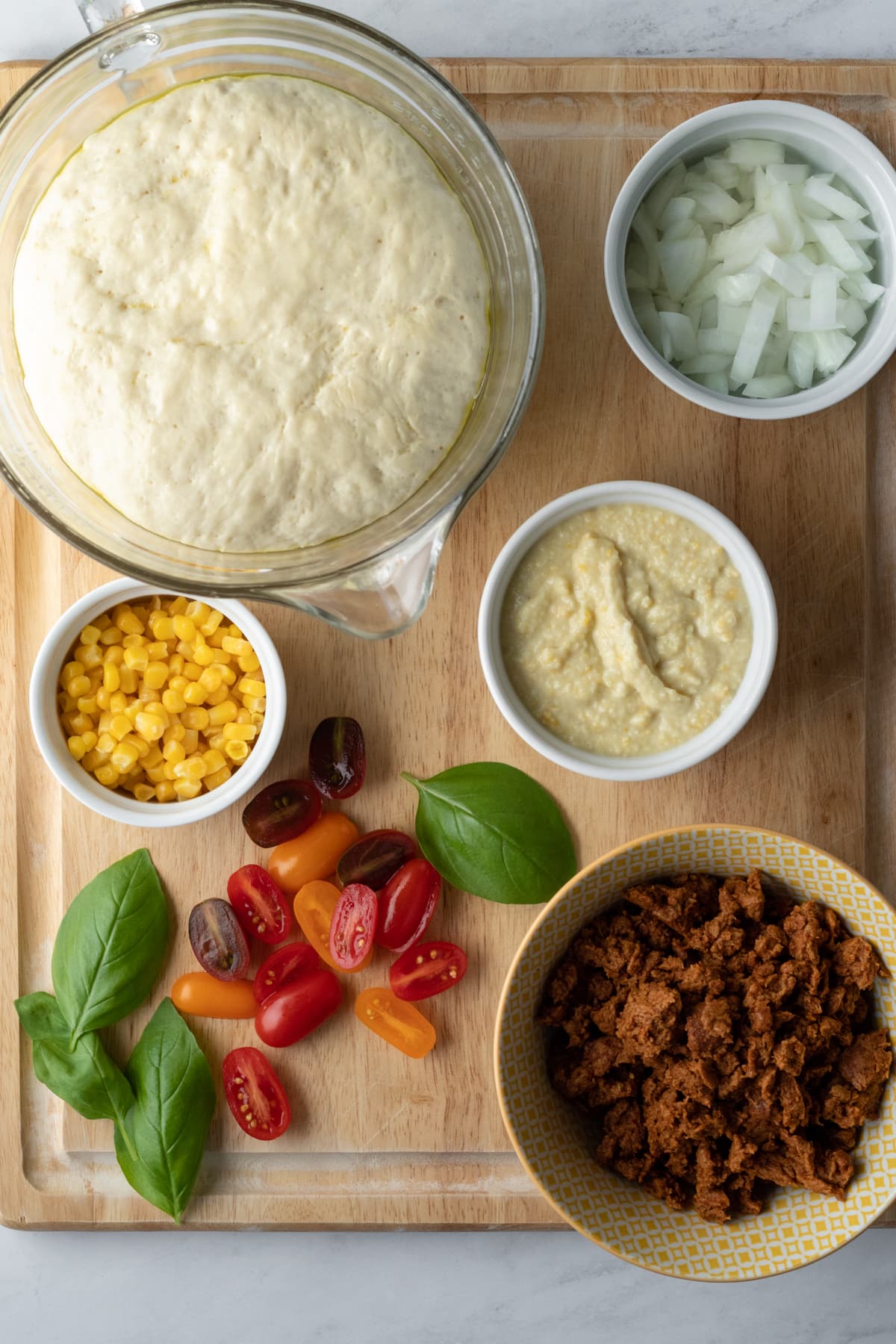 ingredients on a cutting board - dough, onion, creamed corn sauce, vegan chorizo, tomatoes, corn