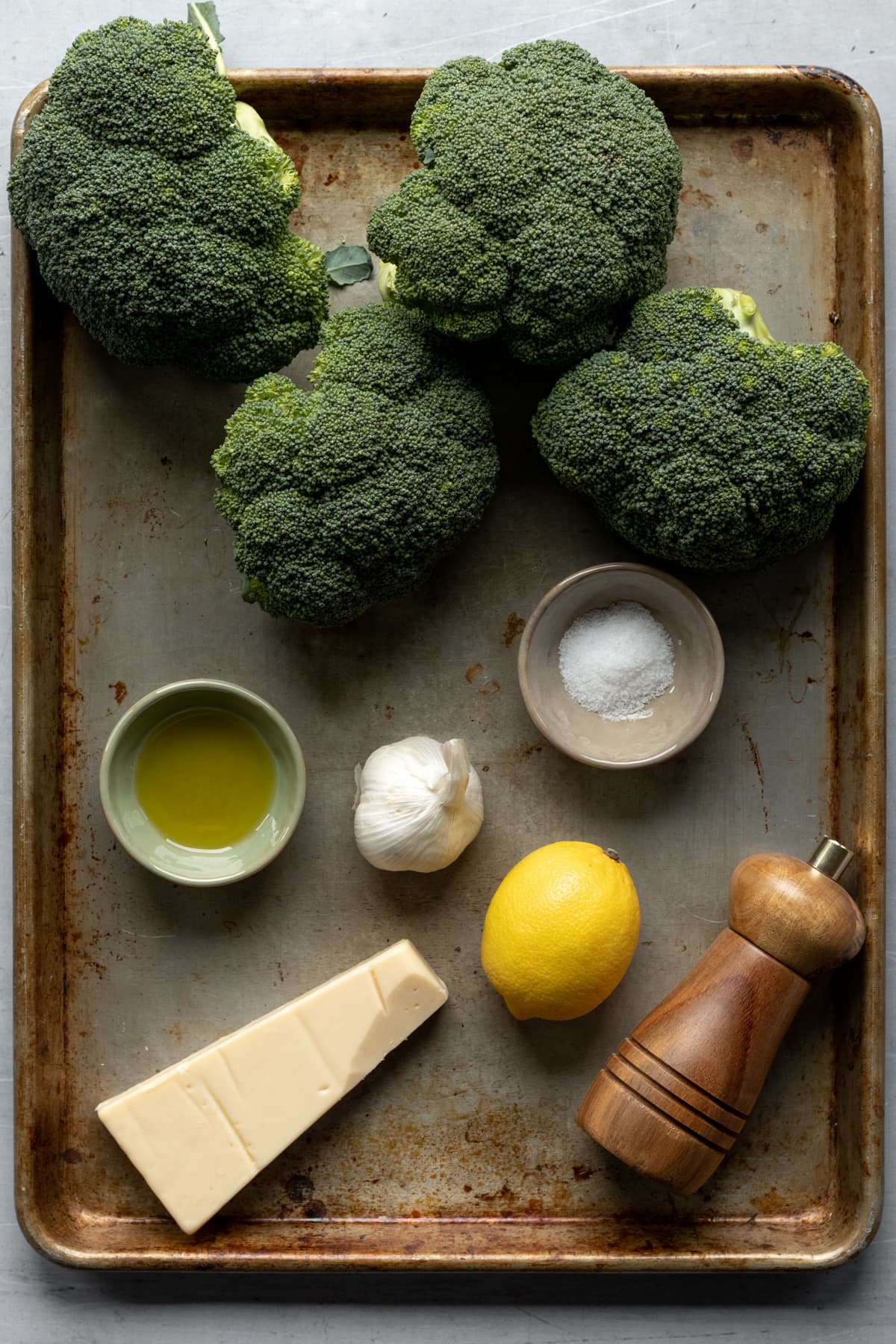 broccoli, garlic, lemon, oil, salt, pepper, and vegan cheese on a baking sheet.