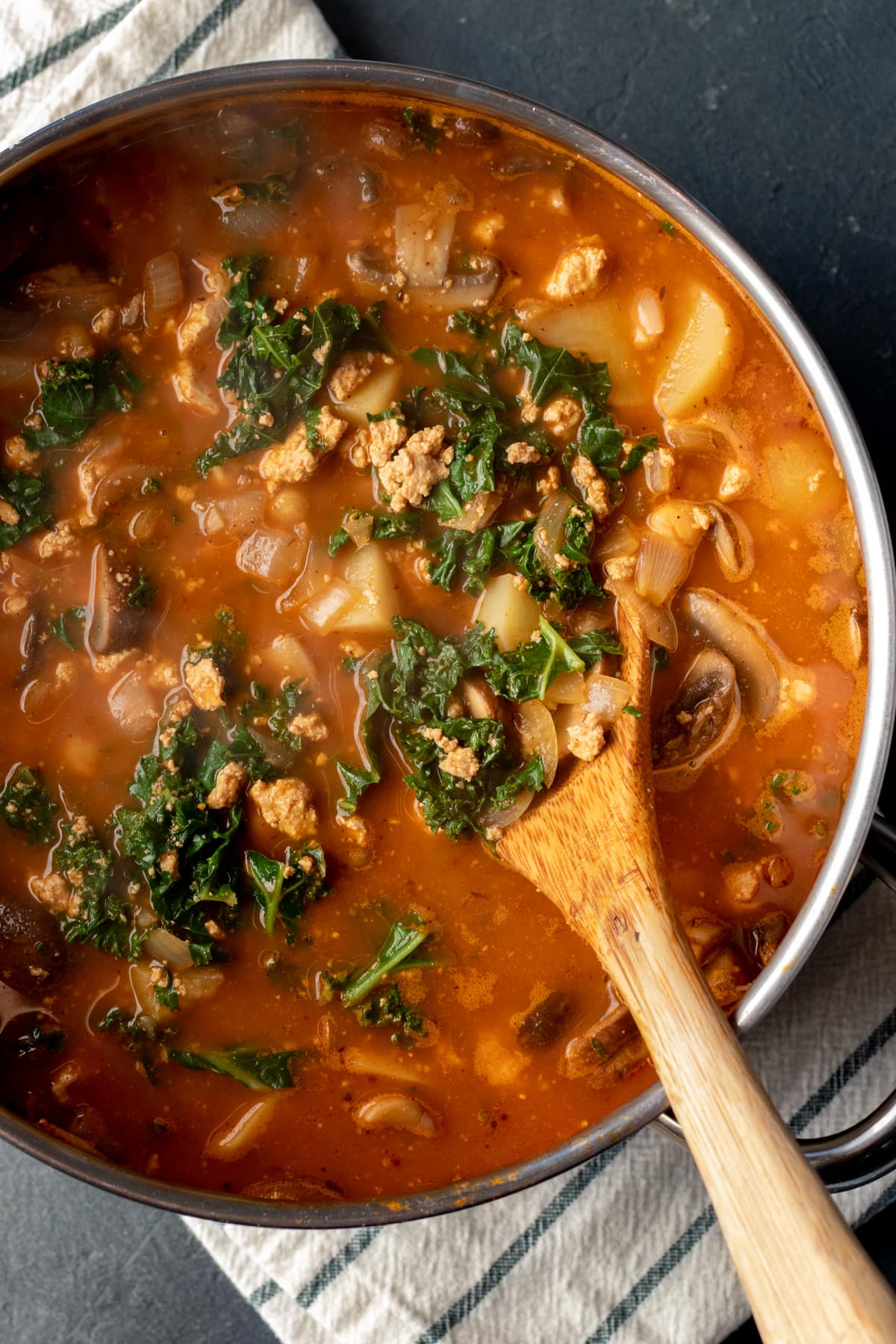 pot full of spicy red soup filled with kale, potato, and tofu chorizo.