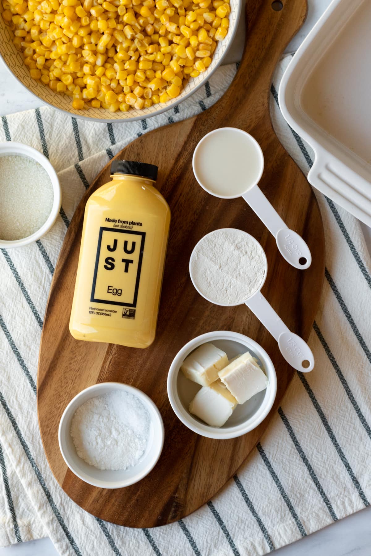 The 7 ingredients needed for vegan corn casserole laid out on a wood board.