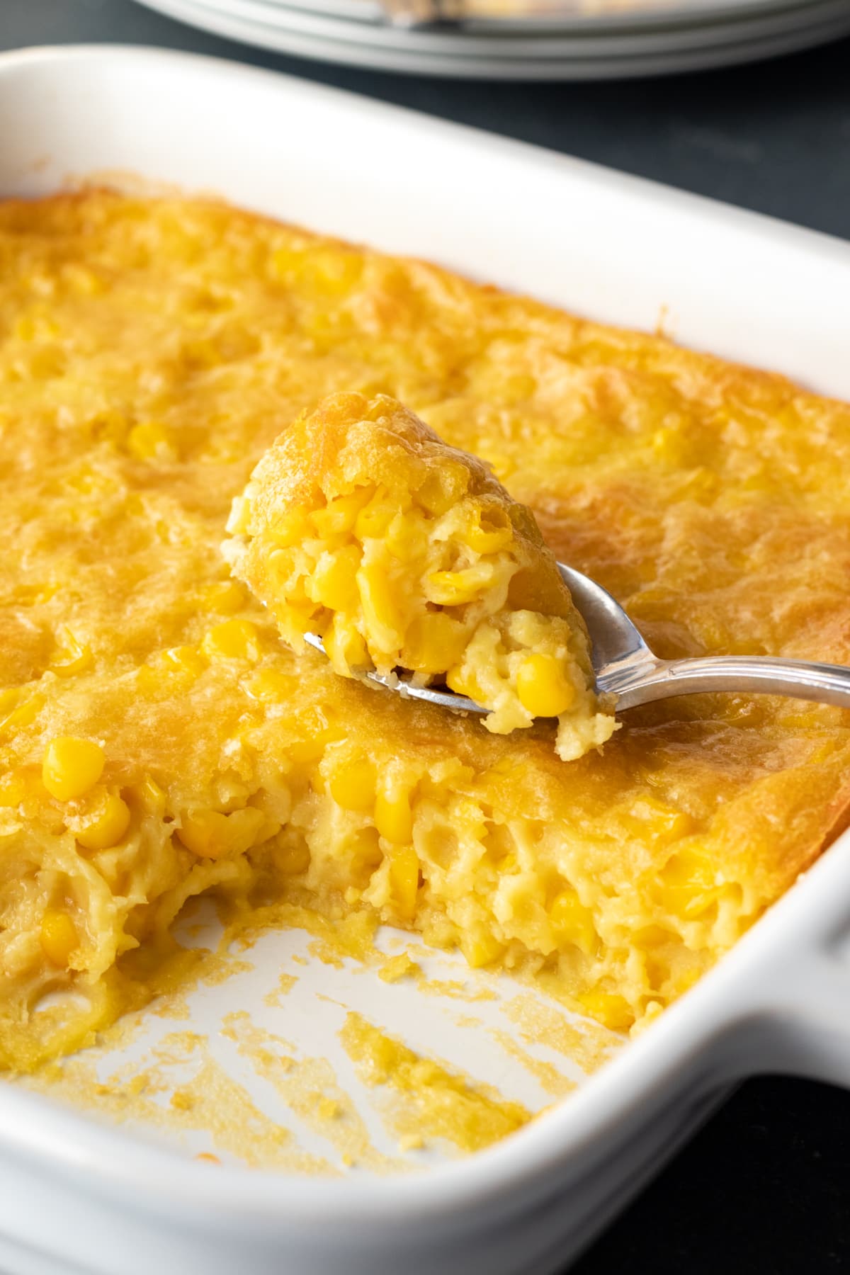 Scooping up corn pudding from a white baking dish.