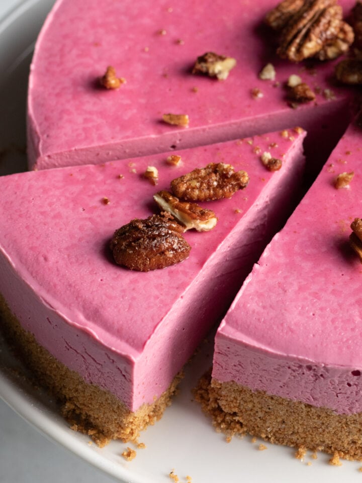 close up of pink cheesecake topped with candied pecans