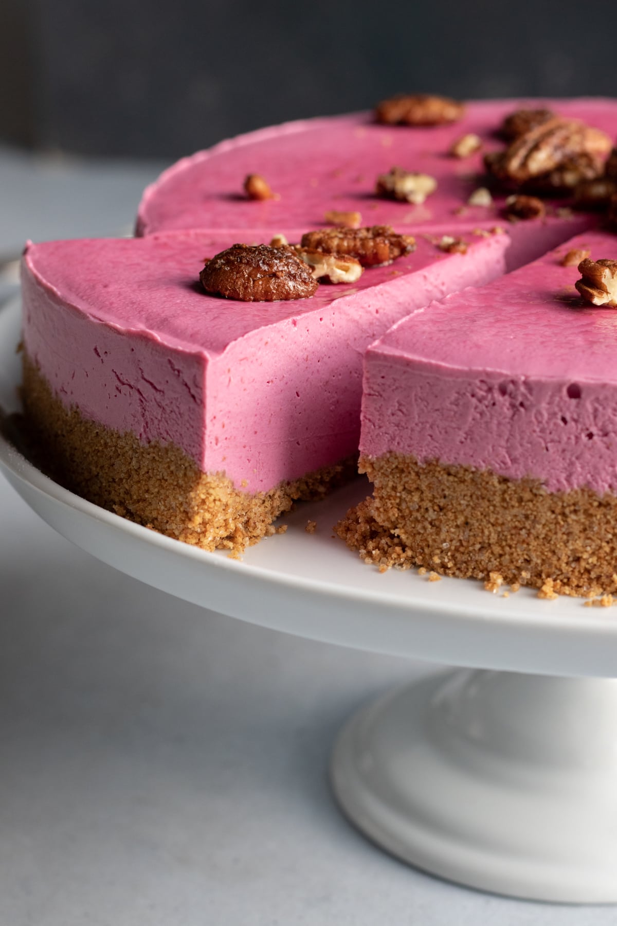 naturally pink cranberry cheesecake with graham crust on a white cake stand.