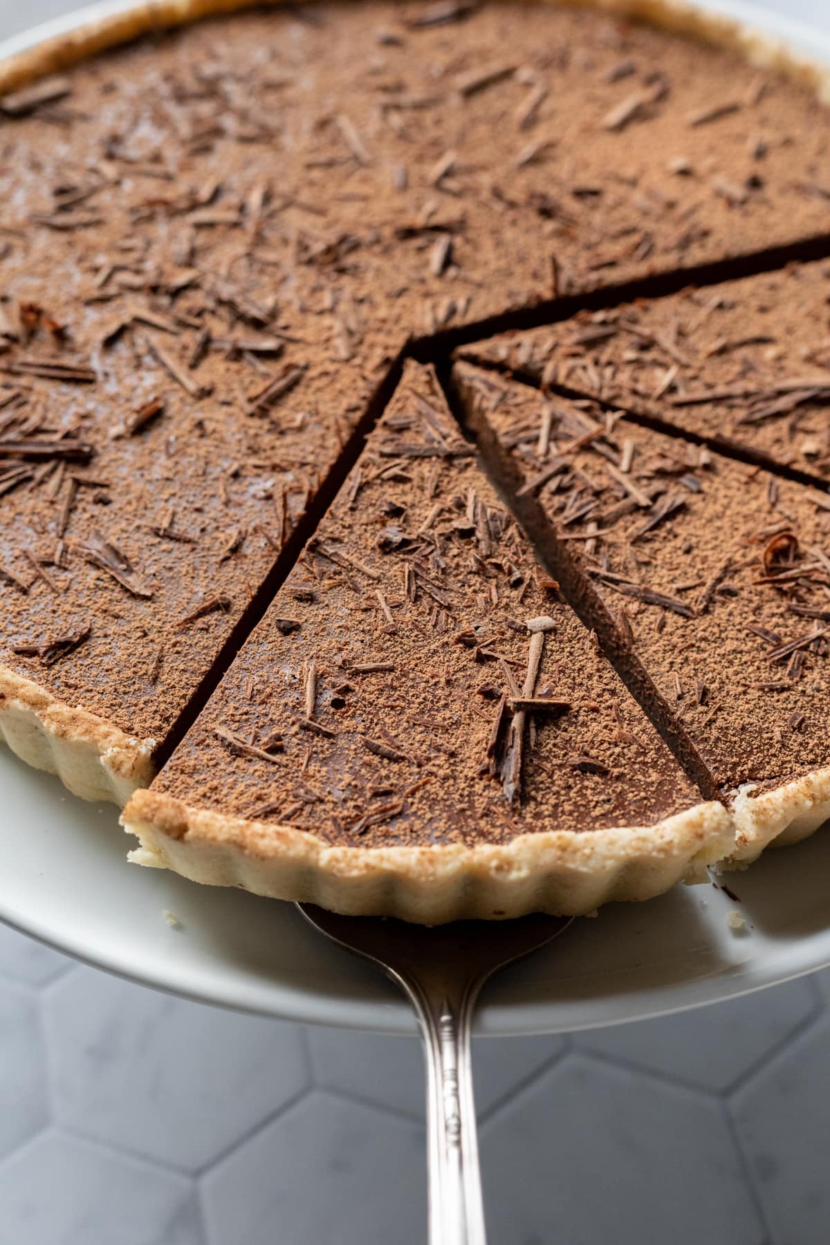 close up of dairy free chocolate tart covered with cocoa powder and chocolate shavings.