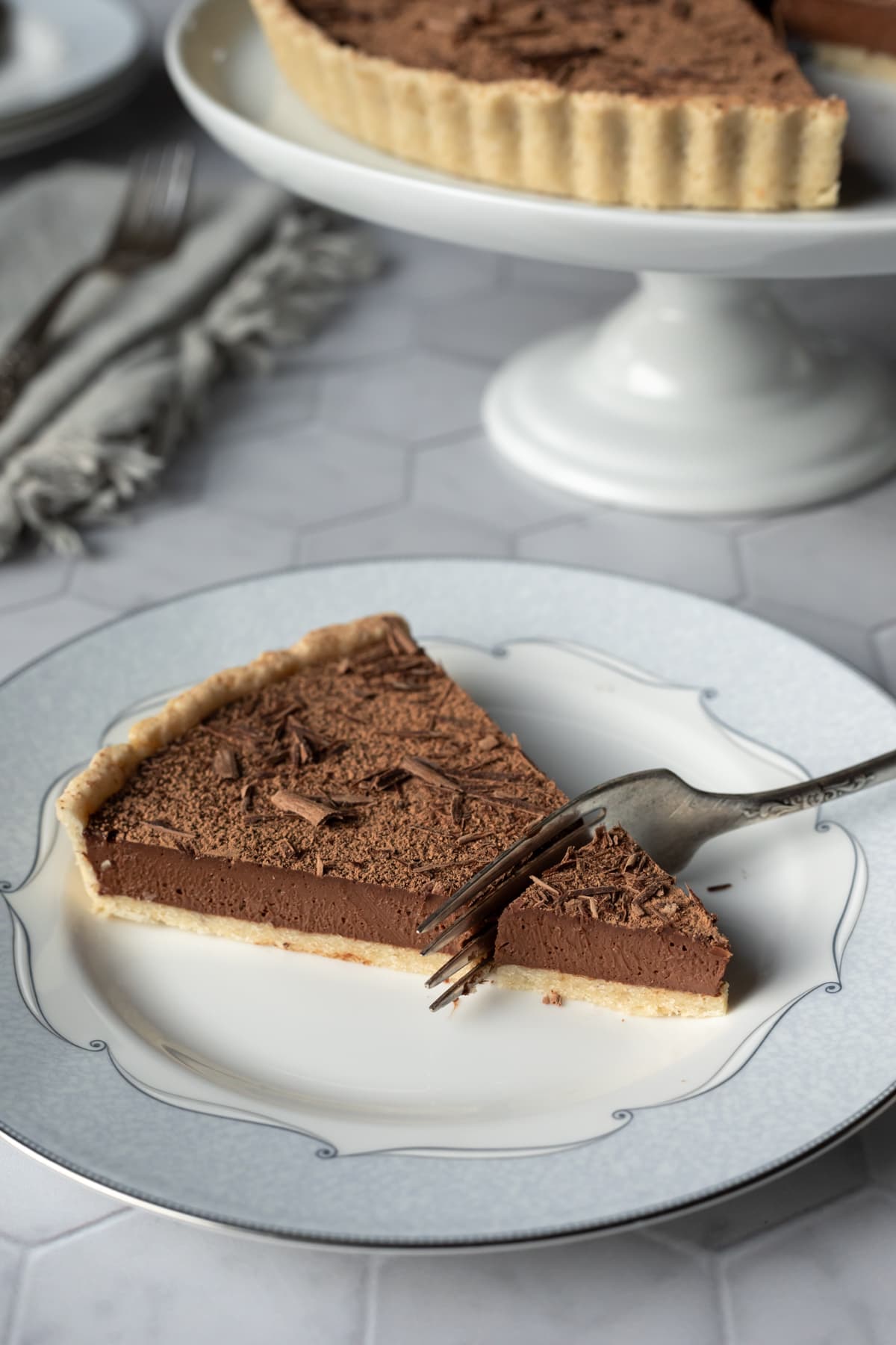 a fork cutting into a slice of chocolate tart on a small plate.