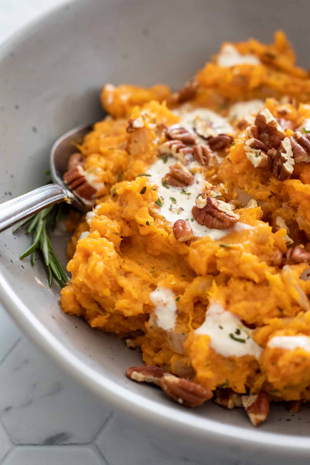 close up photo of finished sweet potato recipe with pecans and a sprig of rosemary.