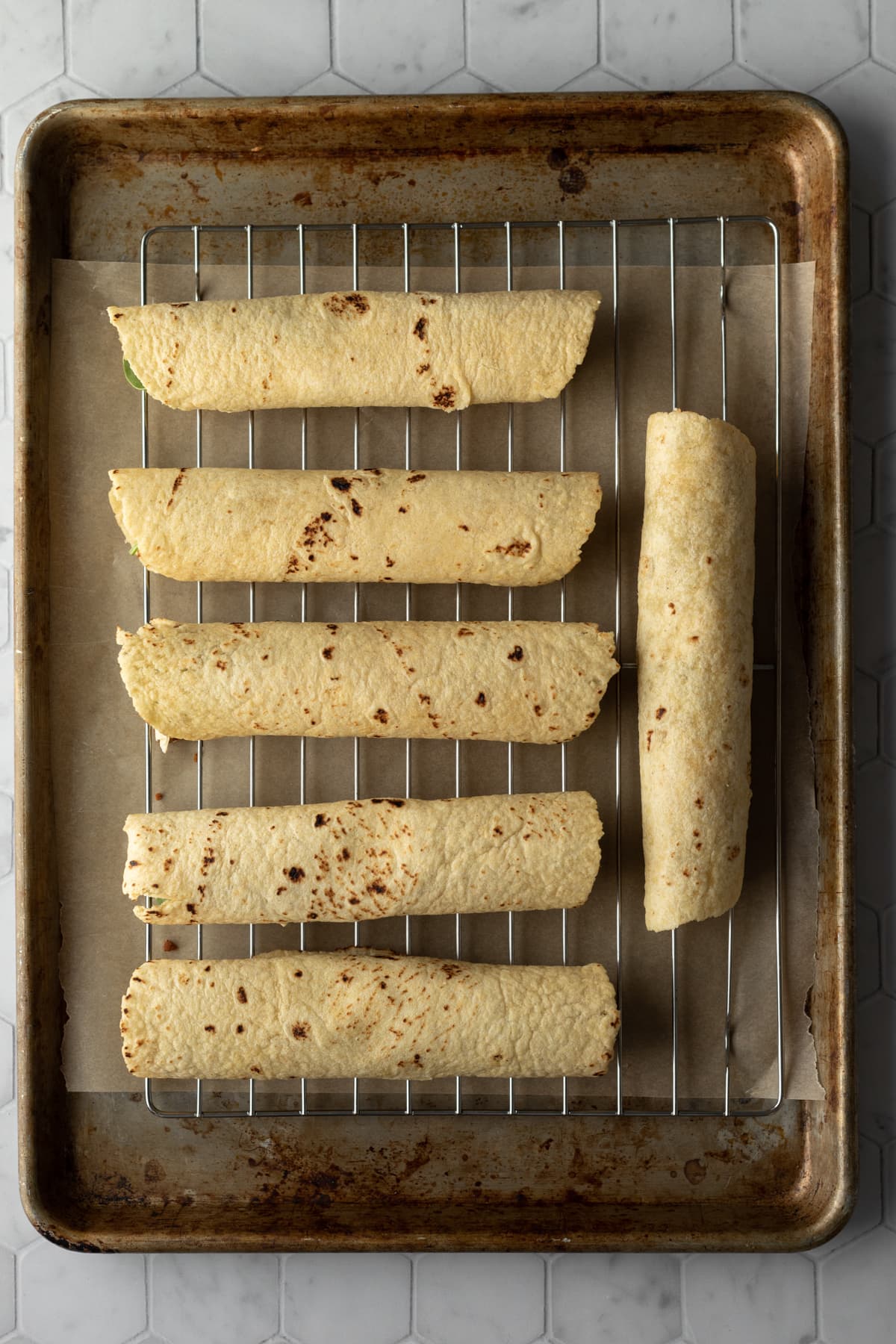 rolled taquitos lined up on a baking sheet.