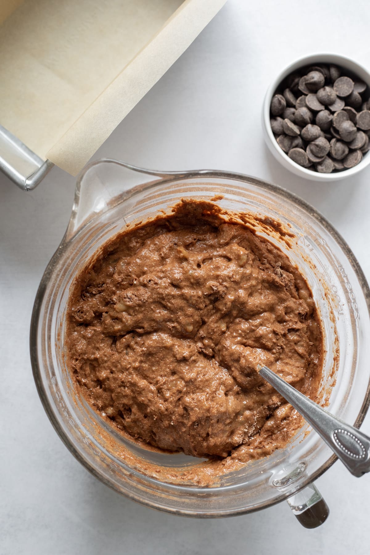 batter in a bowl with chocolate chips and parchment-lined pan to the side.