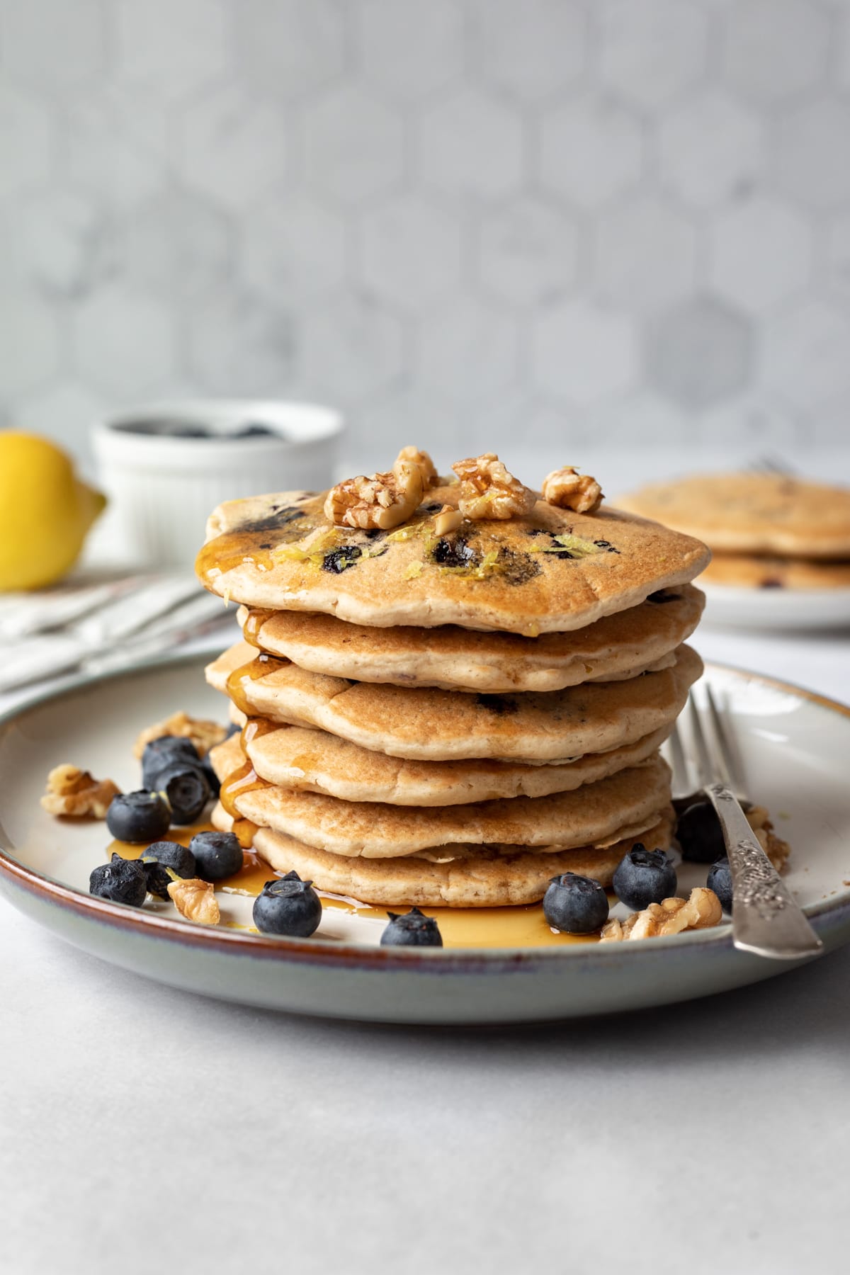 a stack of 6 pancakes topped with walnuts, blueberries, and syrup.