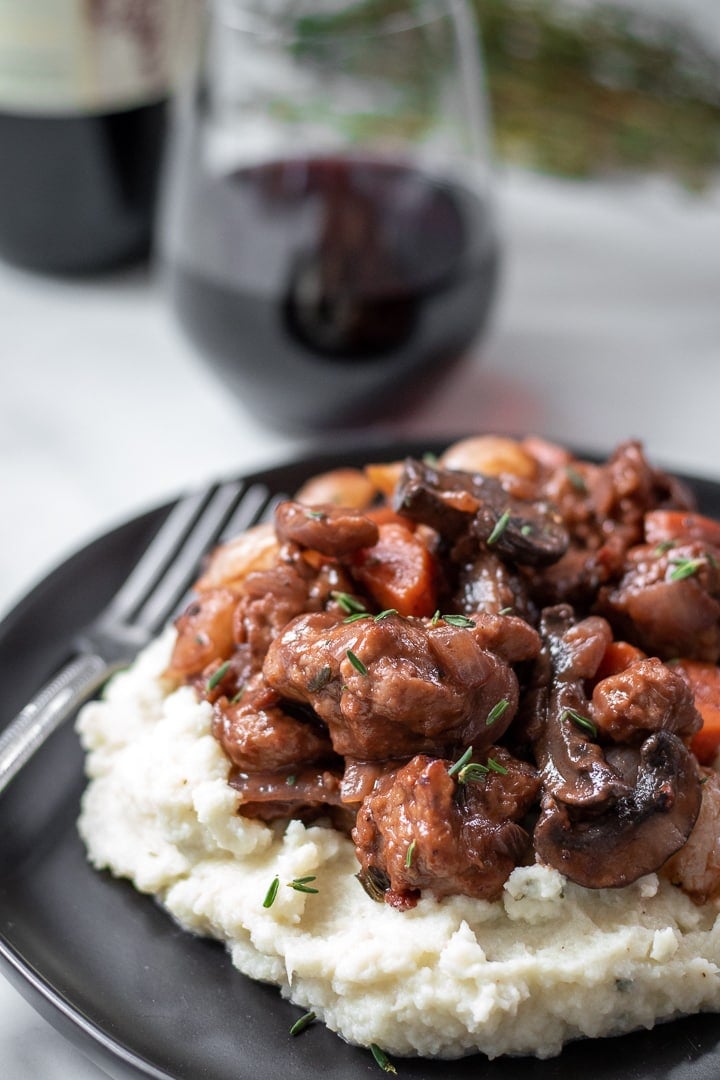 chunky seitan in red wine sauce on a pile of mashed cauliflower.