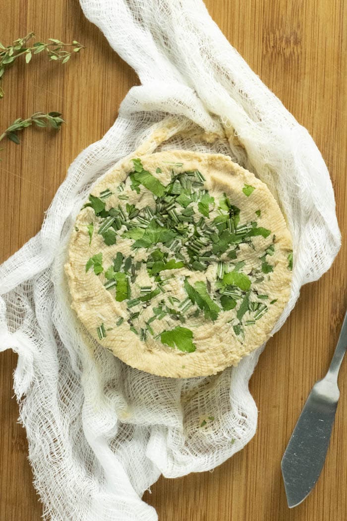 a wheel of vegan cream cheese topped with chopped herbs.