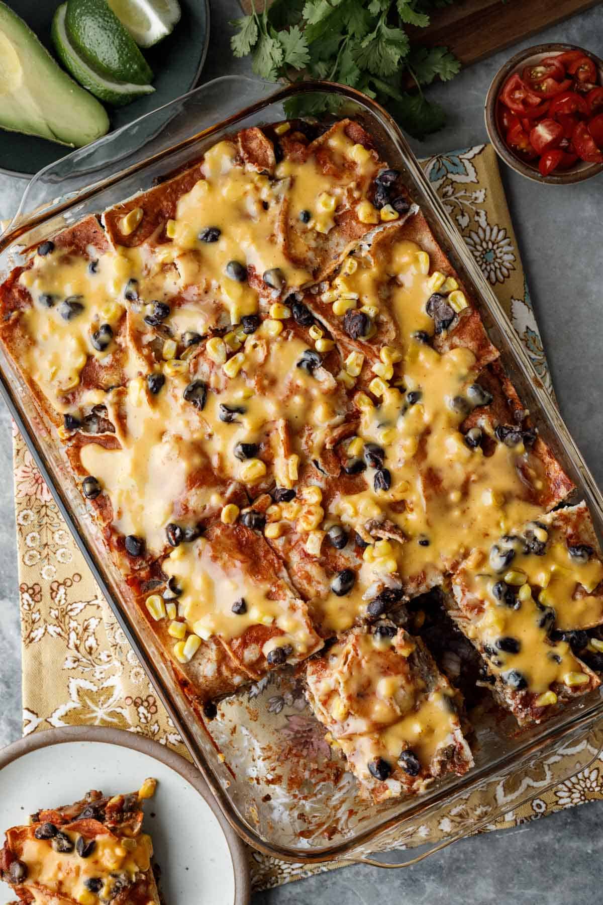 Cheesy vegan enchilada casserole in a glass dish with a serving on a plate.