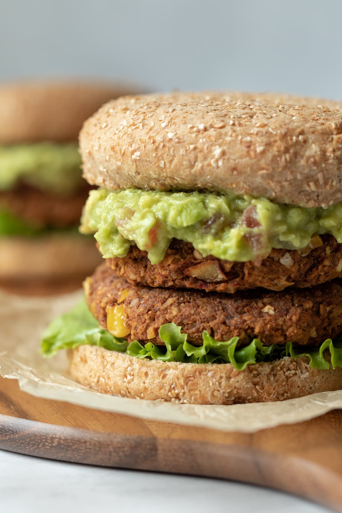 two vegan chickpea burgers stacked on a bun and topped with guacamole.