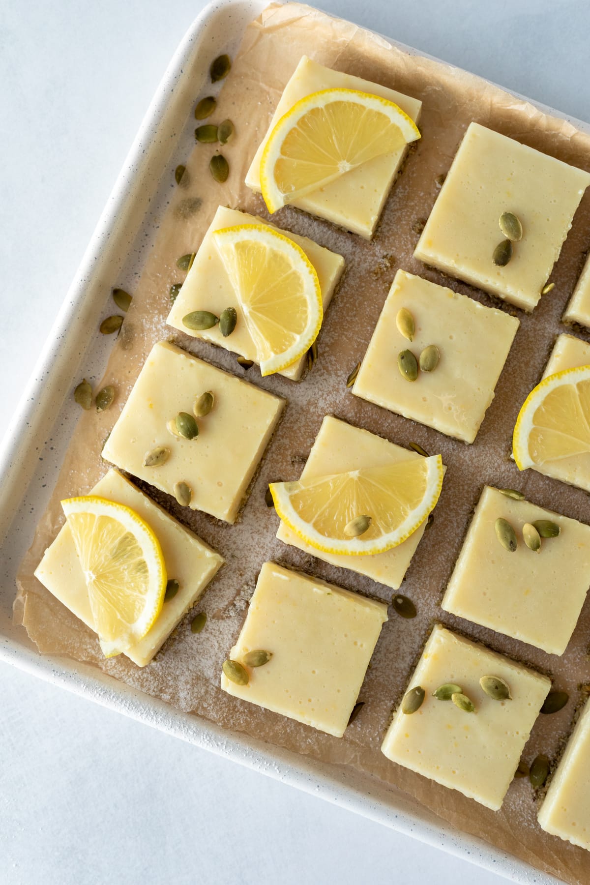 lemon bars sprinkled with pumpkin seeds on a baking sheet.